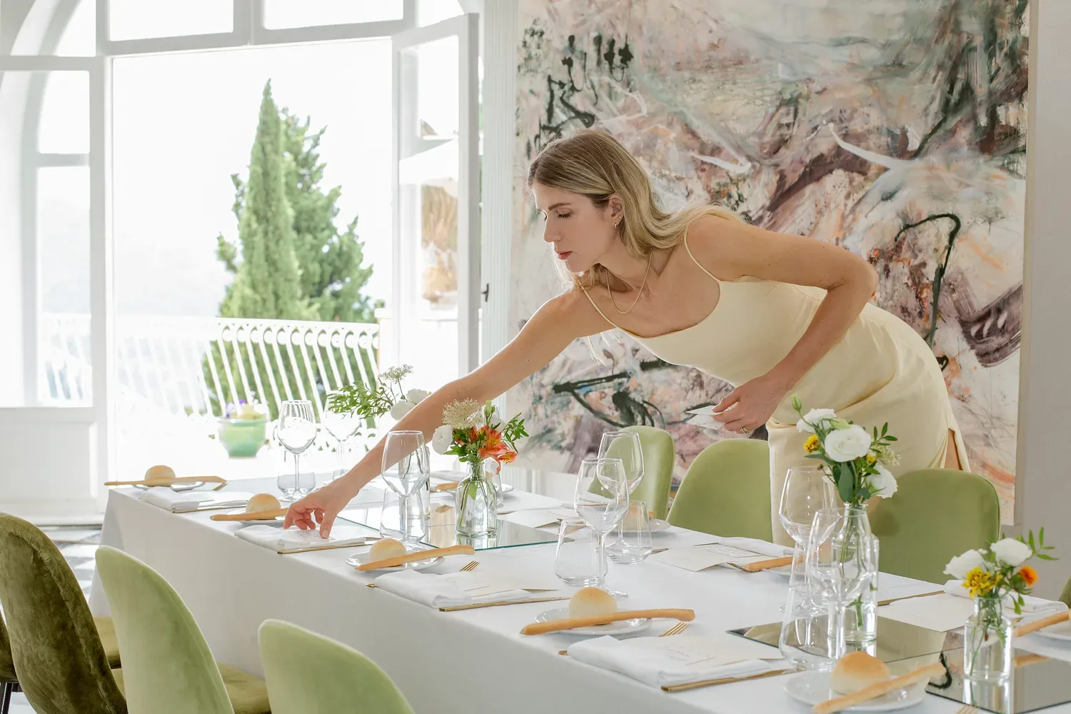 Maria-Theresia Mathisen setting the long table in the salon at Castel Caramel, beneath a large painting